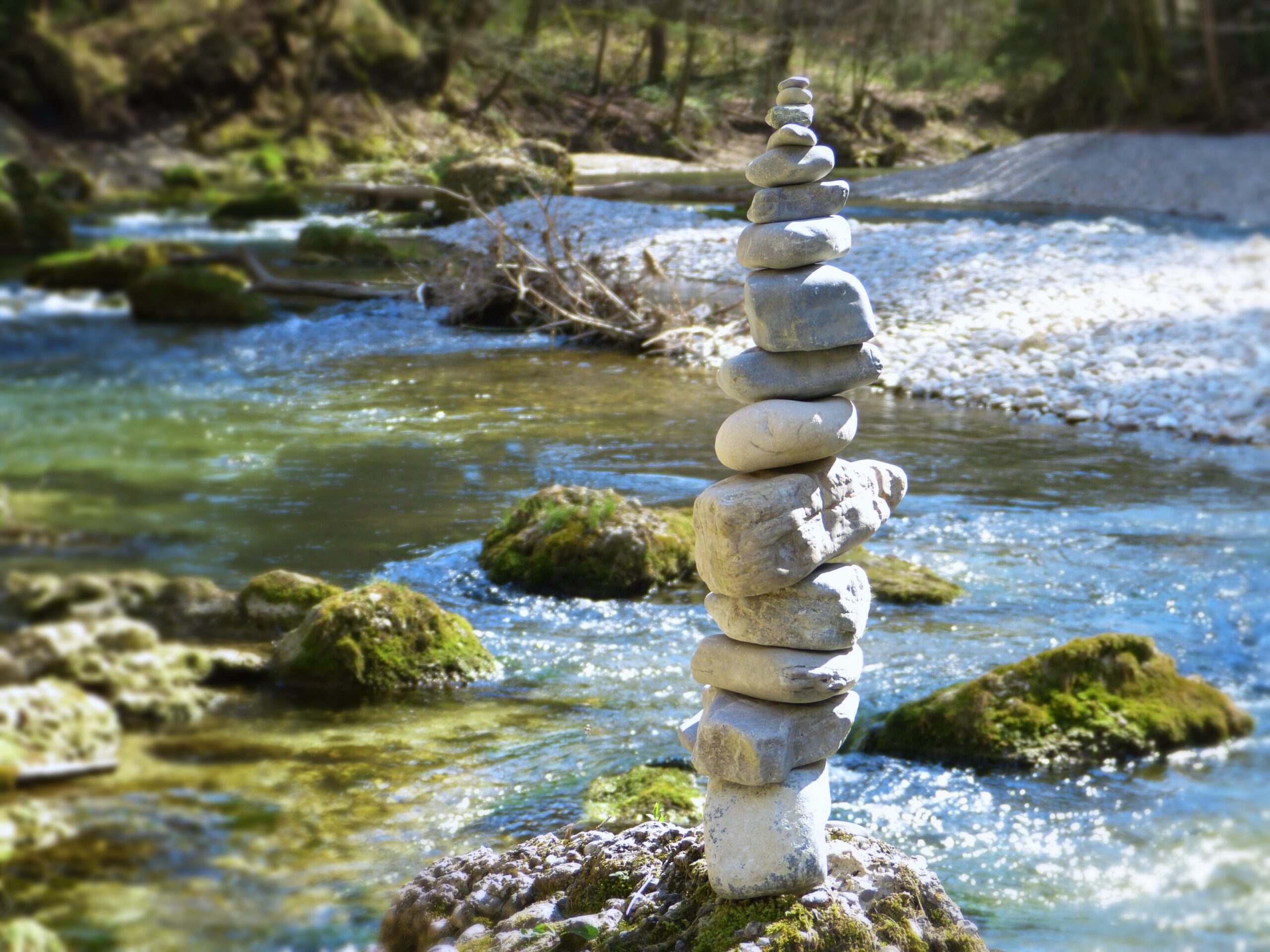 Balanced stack of smooth stones beside a flowing creek, symbolizing mindfulness, emotional balance, and inner peace in therapy